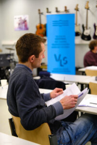 Man met opengeslagen papieren map die aan het luisteren is naar presentatie tijdens een bijeenkomst voor muziekdocenten